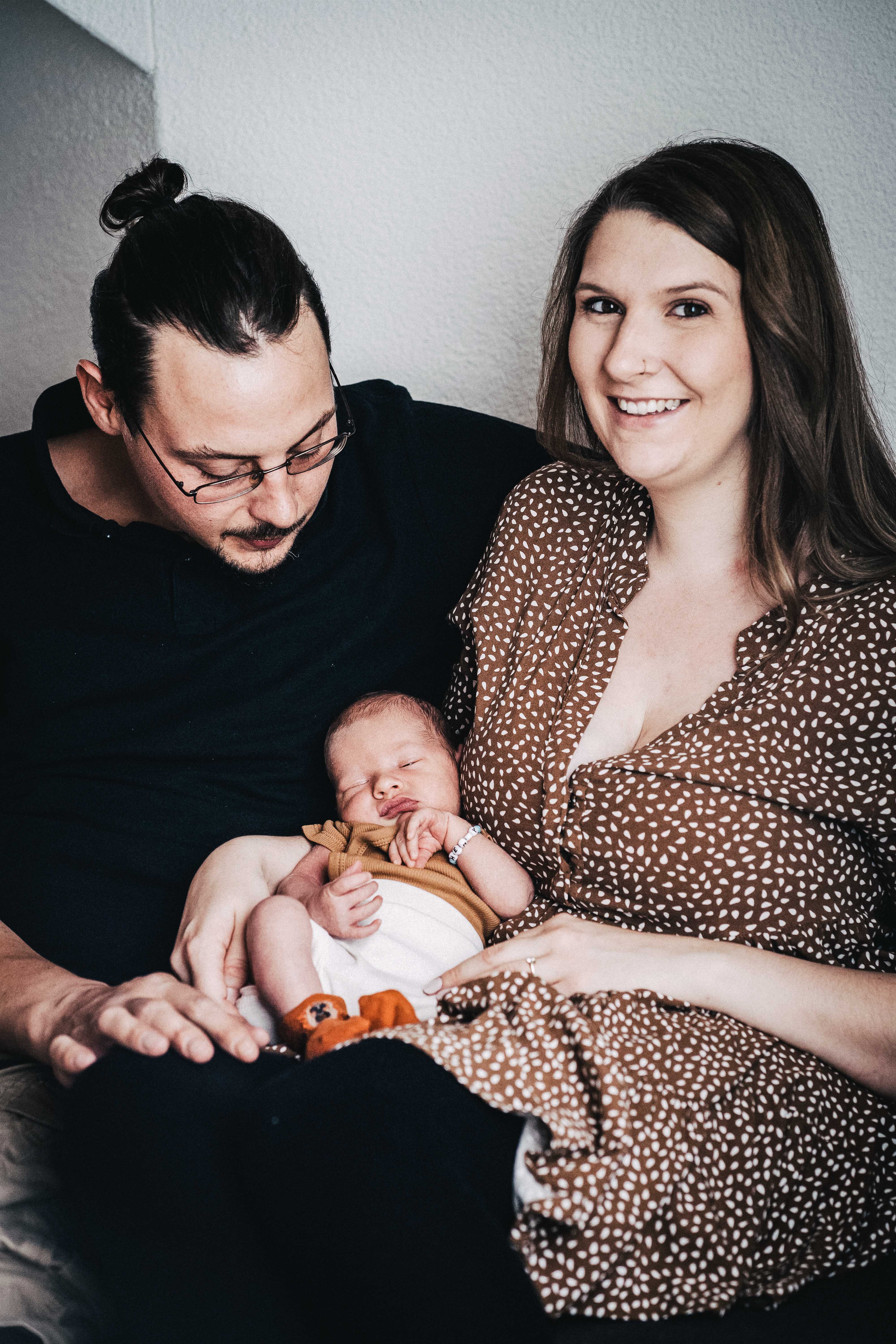 Mutter und Vater sitzen mit Baby im Arm auf einem Sofa