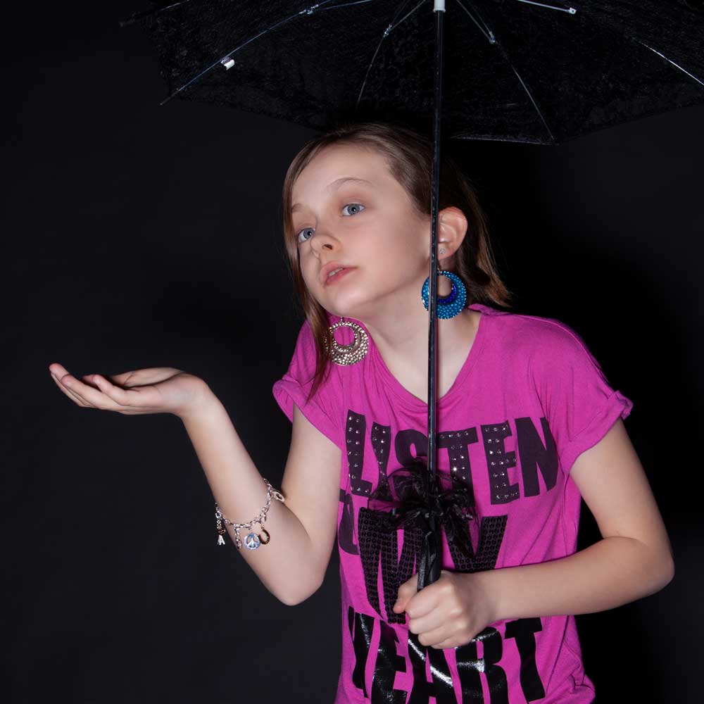 maedchen mit pinkem shirt und regenschirm im studio vor schwarzem hintergrung