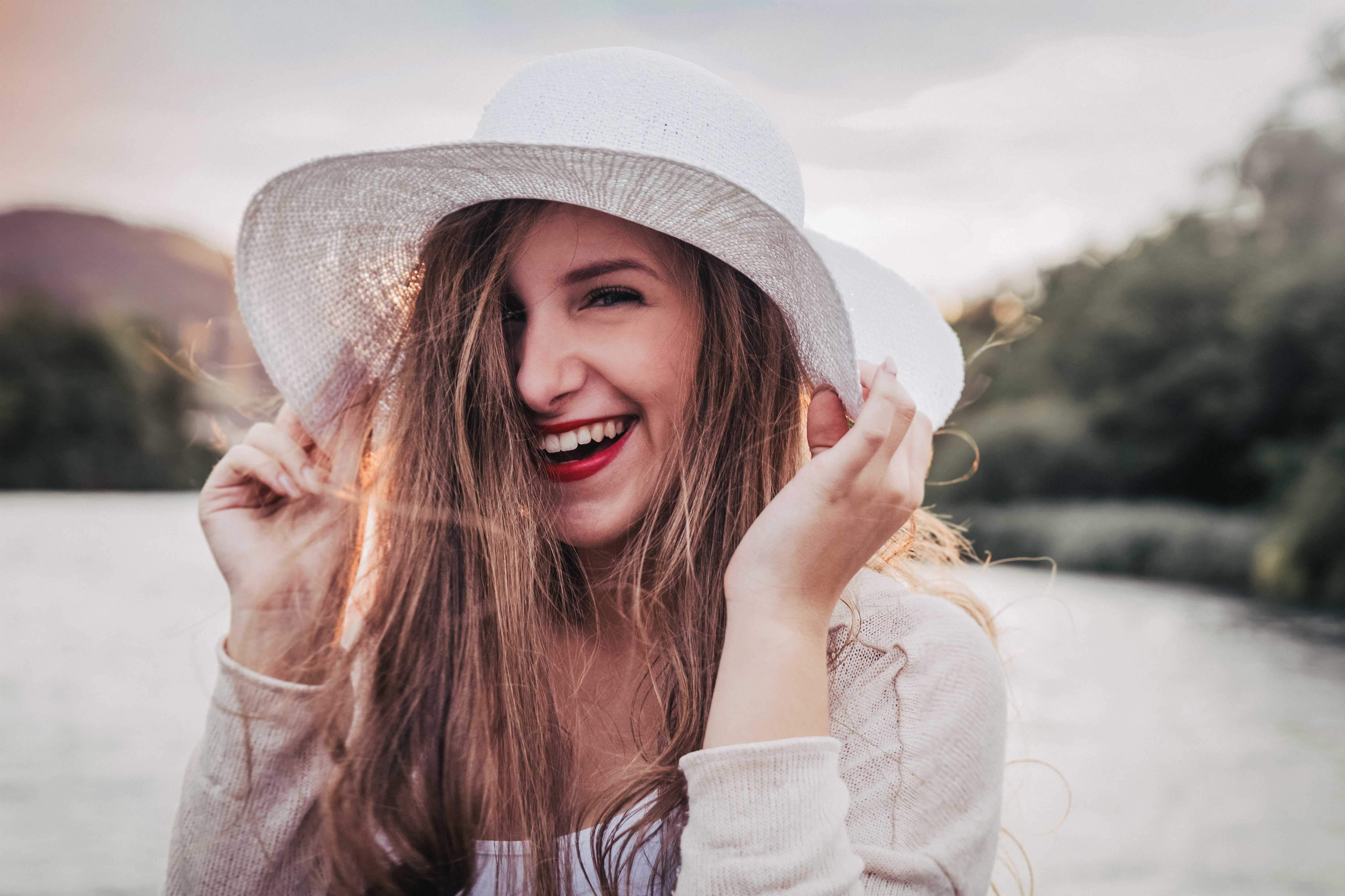 Ein Portraitfoto einer jungen Frau am See mit einem Hut.